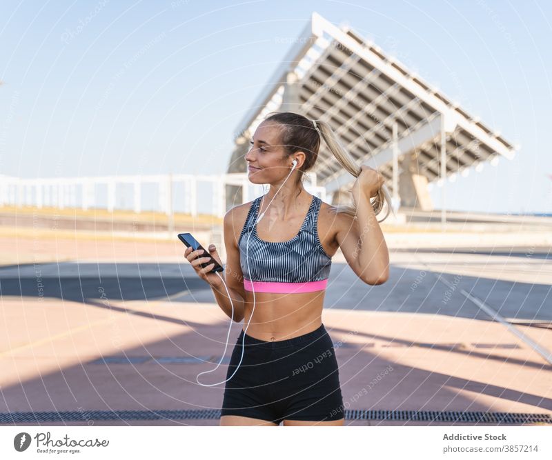 Cheerful sportswoman listening to music in earphones training smartphone enjoy summer female workout city athlete slim healthy fitness happy sporty street smile