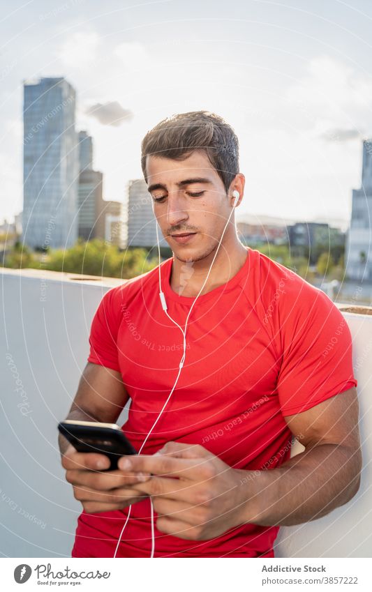 Sportive man with earphones before workout on street sportsman smartphone prepare urban listen training young muscular athlete fitness device gadget music male