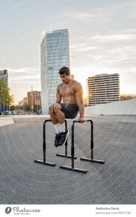 Shirtless sportsman working out on bars in town exercise workout training muscular shirtless balance fit professional endurance city pavement roadway sky