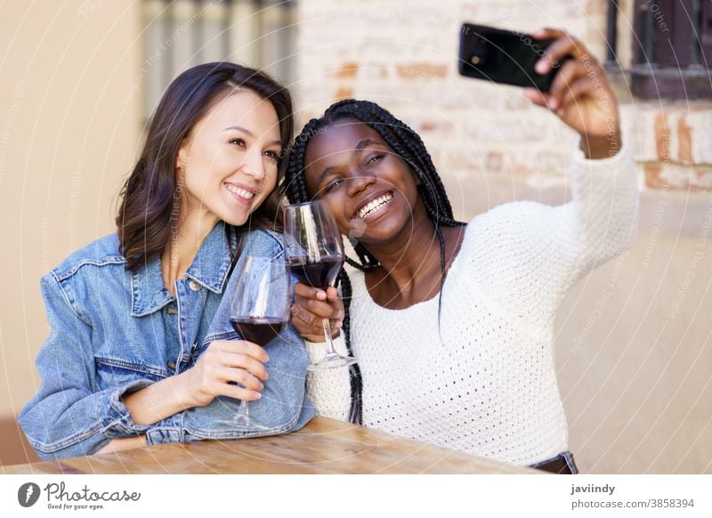 Two women making a selfie with a smartphone while having a glass of wine. woman bar outdoors multiracial happiness girl friendship happy smile young beautiful