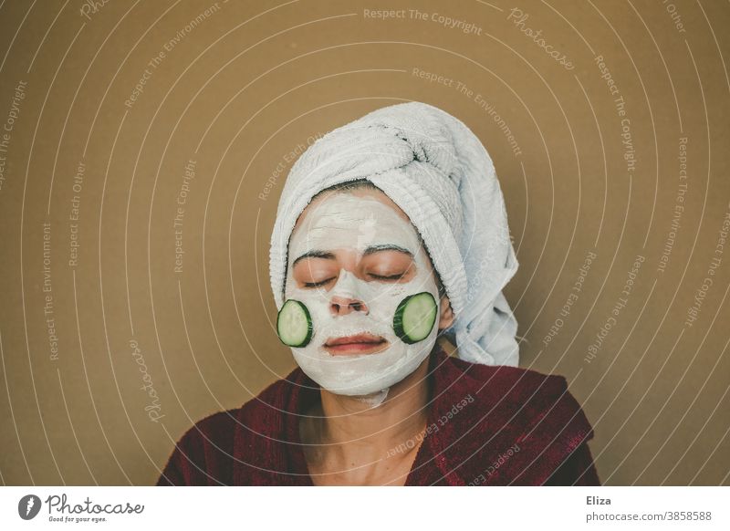 A woman in a bathrobe and towel turban makes a face mask and enjoys it with closed eyes Face mask Cosmetics Skin Personal hygiene Facial care Wellness Spa