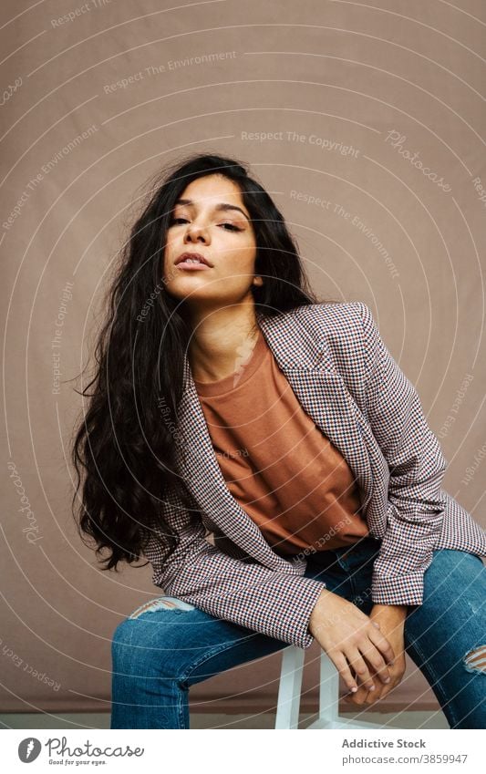 Confident ethnic woman sitting on chair in studio trendy smart casual style model jacket outfit confident female fashion contemporary serious cloth vogue modern