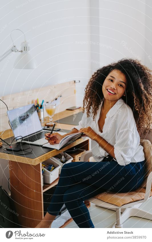 Ethnic woman working remotely from home at home freelance laptop take note write modern planner young african american black ethnic female job gadget device