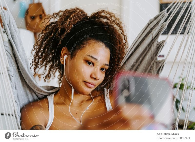 Young black woman with earphones taking selfie at home chill listen smartphone rest using hammock young female african american ethnic music gadget device relax