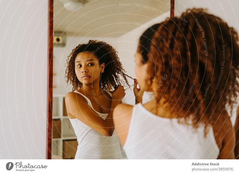 Young ethnic woman adjusting hair near mirror morning at home afro hairstyle routine reflection beauty young african american black female lifestyle curly hair