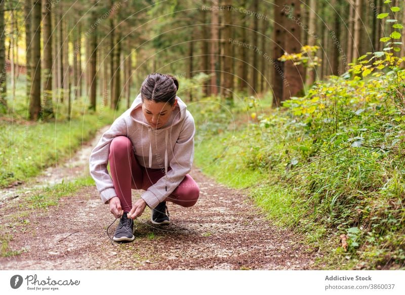 Sporty woman tying shoelaces in forest tie sportswoman sneakers training woods footwear athlete fit female activewear fitness workout wellness break path