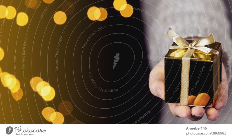 hand holding a gold gift box with gold ribbon,bokeh sparkle background, Christmas or Birthday present concept with space for text holiday surprise celebration