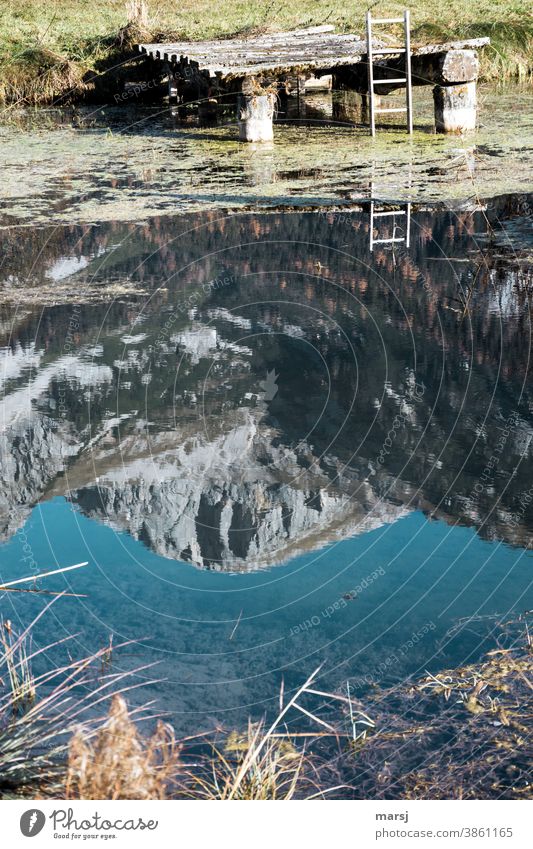 The way out of the sunken mountain world. Reflection of the Sinabell in a fish pond with landing stage and exit ladder Water Alps Harmonious Calm Meditation