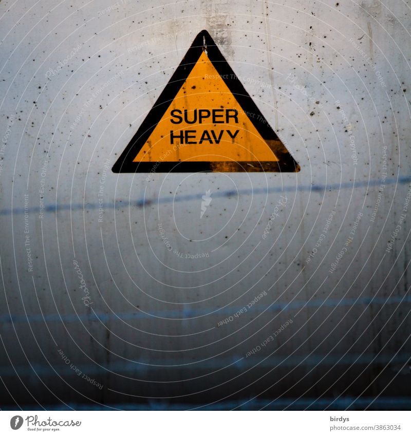 Super heavy, warning sign on a heavy concrete element, barbed wire in the foreground.weight, overweight. Extreme Warn Triangle Concrete Heavy super heavy