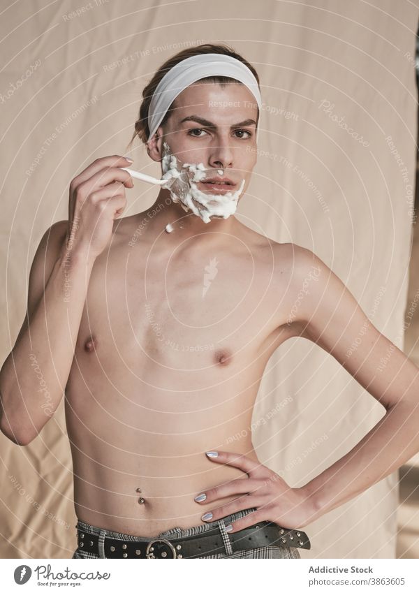 Androgynous young man shaving face shave androgynous transgender hygiene grooming prepare razor shirtless slim male manicure foam skin care hand on waist queer