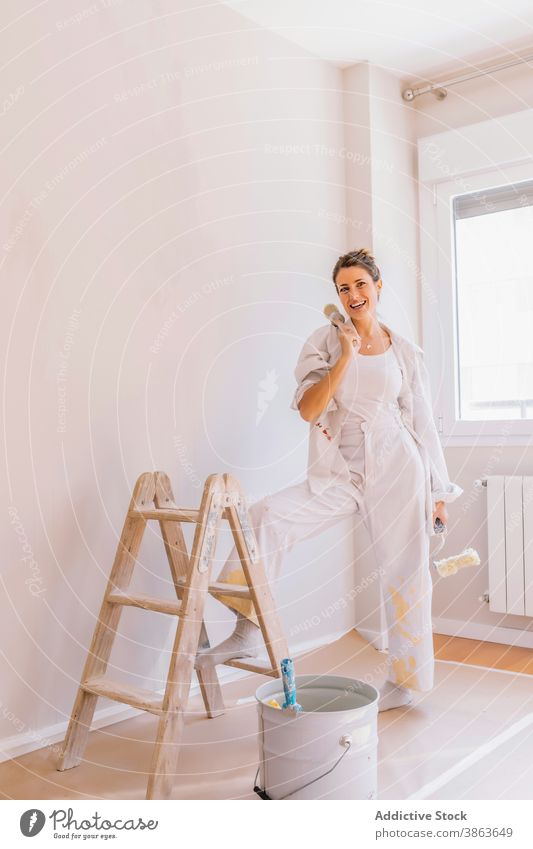 Cheerful woman preparing paint during renovation bucket renovate home smile paintbrush wall prepare apartment female young happy floor kneel flat contemporary