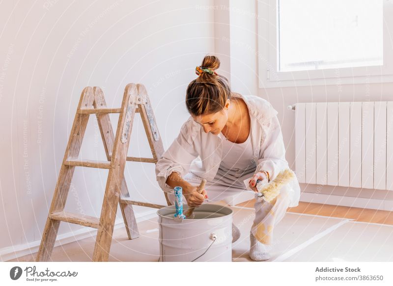 Cheerful woman preparing paint during renovation bucket renovate home smile paintbrush wall prepare apartment female young happy floor kneel flat contemporary