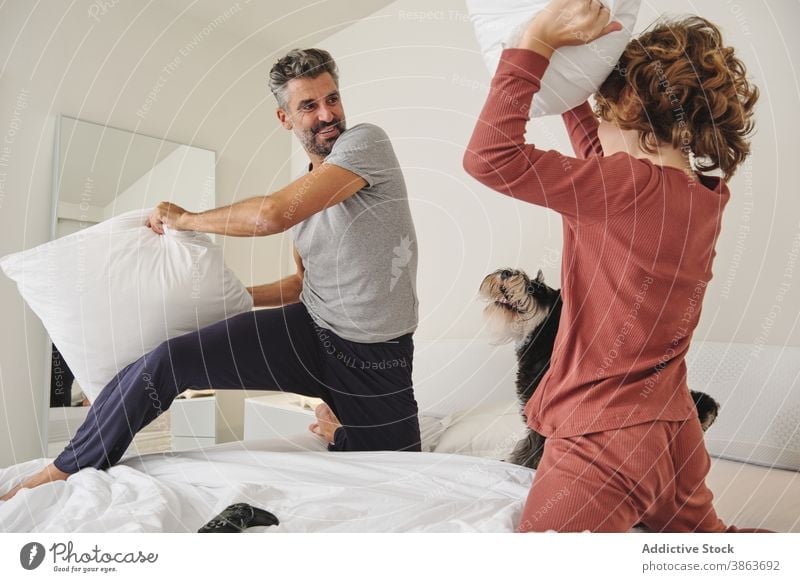 Carefree man and boy jumping on bed during pillow fight having fun father son together play game carefree home cheerful kid happy relationship parent playful