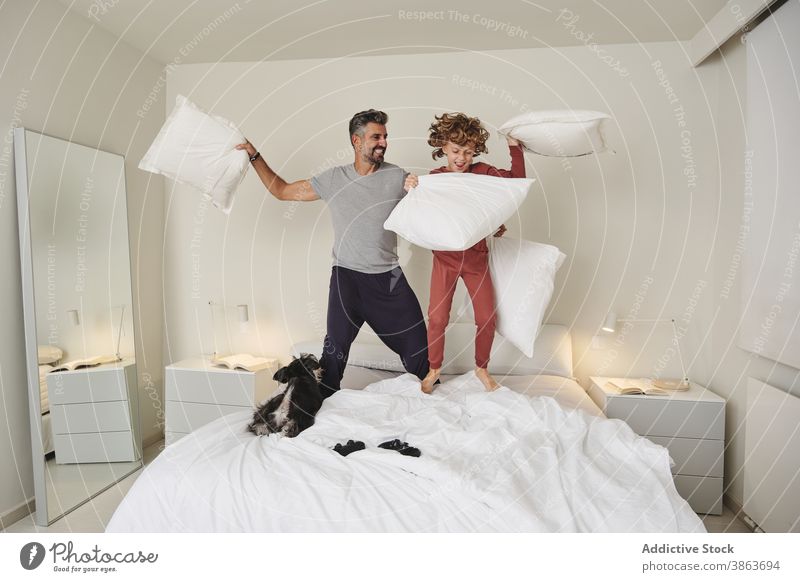 Carefree man and boy jumping on bed during pillow fight having fun father son together play game carefree home cheerful kid happy relationship parent playful