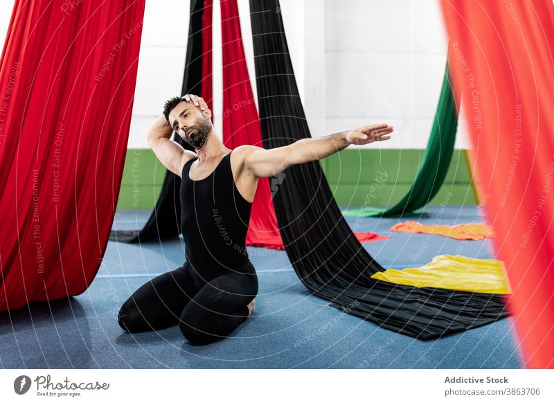 Male dancer stretching neck near aerial silks man warm up rehearsal studio tilt flexible male adult outstretch fabric kneel cloth colorful leotard professional