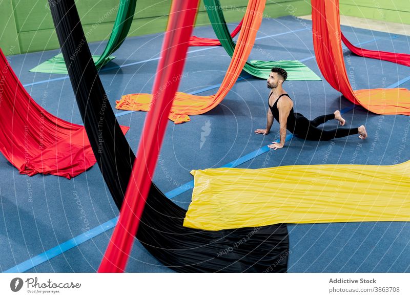 Male gymnast stretching near colorful pieces of cloth man dancer studio rehearsal aerial silk flexible bend male adult leotard exercise perform energy practice
