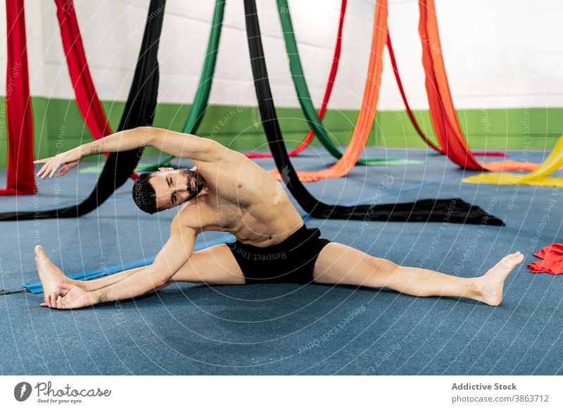 Male dancer stretching near aerial silks man floor studio flexible gymnastic prepare rehearsal male ribbon muscular barefoot bend split cloth practice exercise