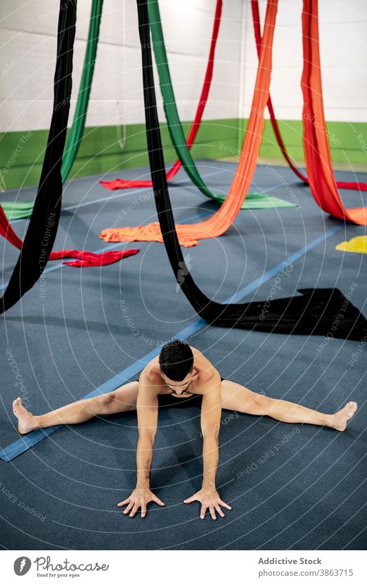 Male dancer stretching near aerial silks man floor studio flexible gymnastic prepare rehearsal male ribbon muscular barefoot bend split cloth practice exercise