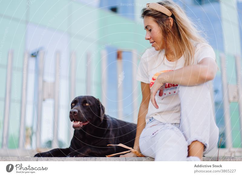 Cheerful woman with black dog in city friendship obedient labrador retriever relax bench summer animal female pet domestic together stroll sit companion smile