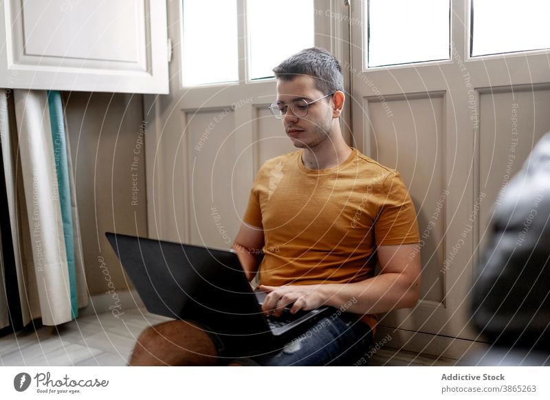 Busy man working on laptop in living room freelance remote home typing project concentrate browsing male casual outfit floor sit window legs crossed device job