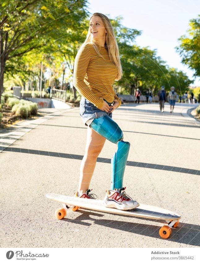 Smiling woman riding longboard in city bionic prosthesis ride skater leg cheerful disable artificial limb female amputee street happy urban optimist town