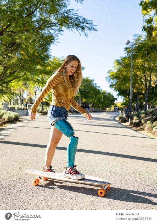 Smiling woman riding longboard in city bionic prosthesis ride skater leg cheerful disable artificial limb female amputee street happy urban optimist town