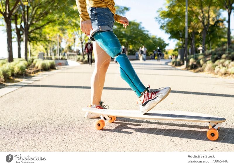 Crop woman riding longboard in city bionic prosthesis ride skater leg cheerful disable artificial limb female amputee street urban optimist town skateboard