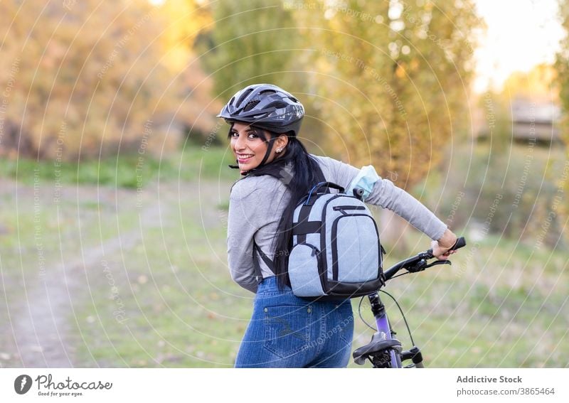 Positive woman with bike in autumn countryside bicycle forest active happy nature ride backpack helmet cheerful female smile trail path activity bicyclist