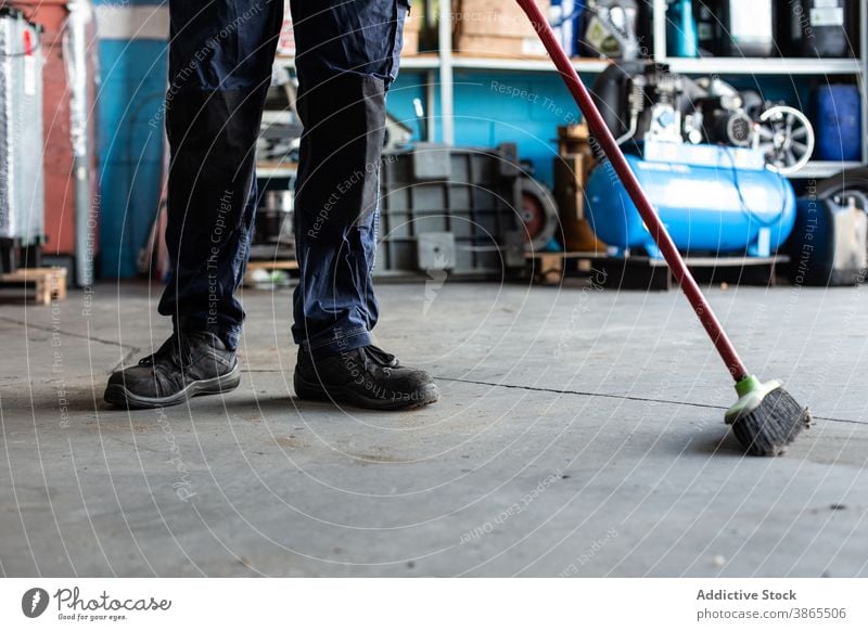 Unrecognizable mechanic sweeping floor in workshop man garage broom clean uniform male job professional service staff employee industry busy labor maintenance