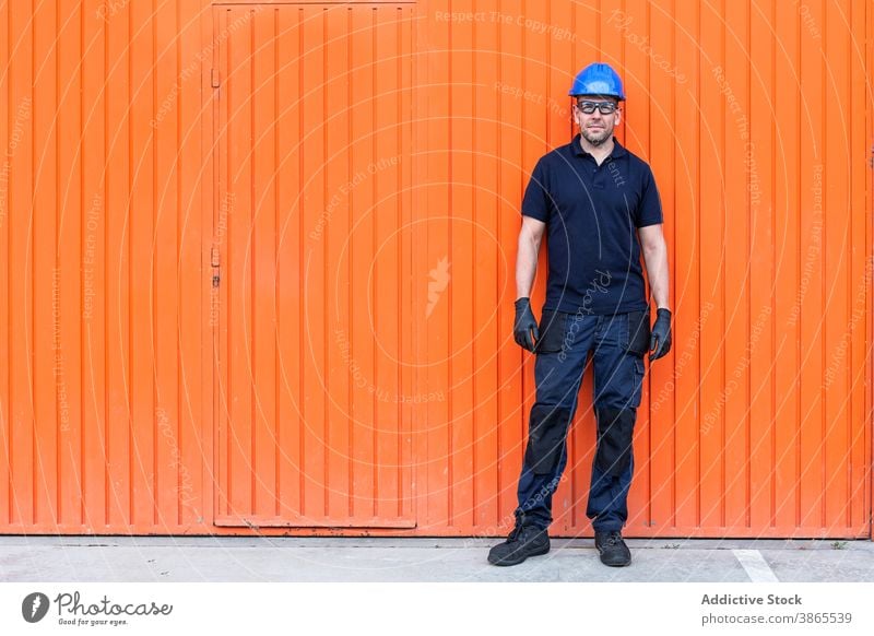 Male worker in hardhat standing near workshop cheerful confident friendly man professional mechanic positive wall adult male workman bright smile job happy