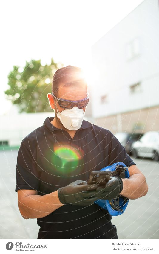 Workman in protective mask using smartphone on street worker mechanic repairman respirator glove break glasses mobile device professional gadget male message