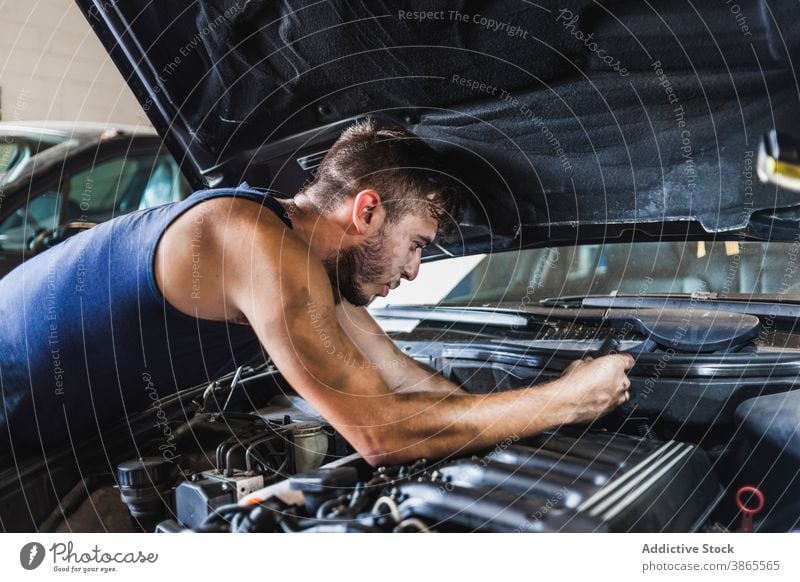 Male mechanic unscrewing engine of car man garage work dirty maintenance repair male fix vehicle transport occupation professional motor automobile screwdriver