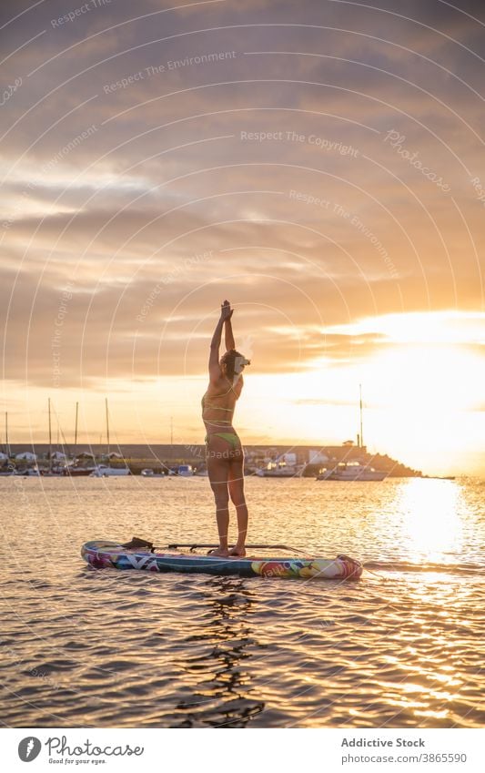 Slim woman practicing yoga on paddle board at sunset mountain urdhva hastasana pose silhouette sea water float paddleboard slim female position stand