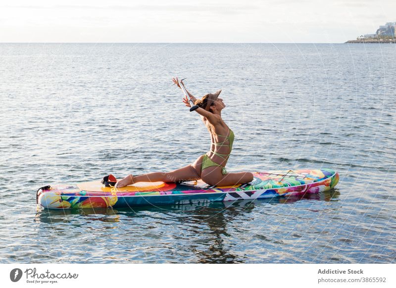Slim woman doing seated yoga pose on paddle board sit half pigeon asana water slim flexible fit female position healthy ardha capotasana practice wellness ocean