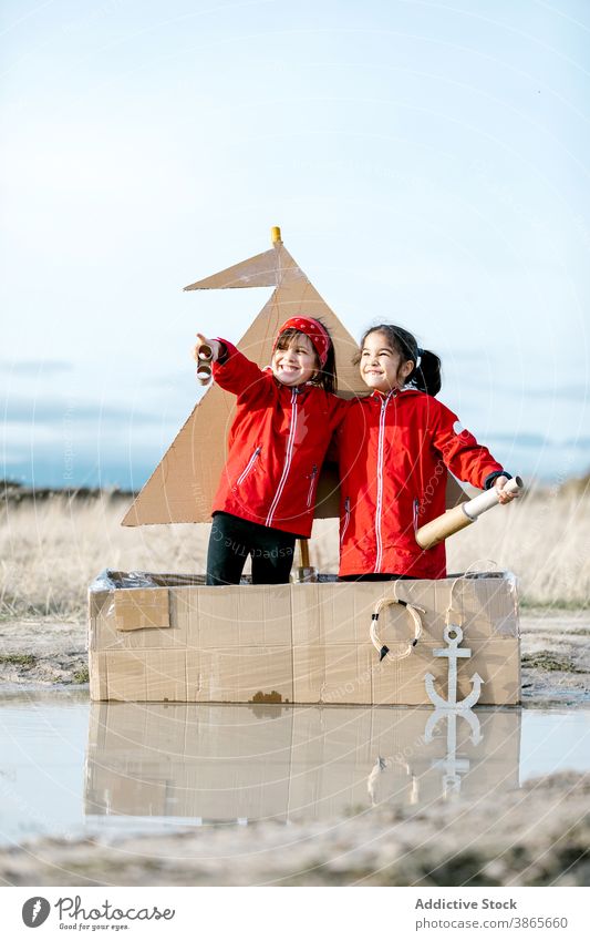 Girls playing in carton boat in puddle cardboard child together having fun imagination game girl spyglass handmade cheerful happy enjoy smile kid childhood