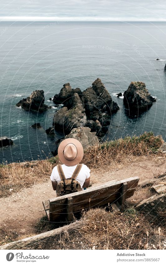 Traveler sitting on bench and enjoying scenic seascape travel man cliff admire scenery hill traveler explore male explorer hat wooden vacation spectacular rock