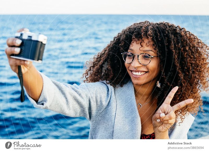 Happy African American female taking selfie near sea woman smile weekend v sign photo camera gesture water shore young ethnic black african american two fingers