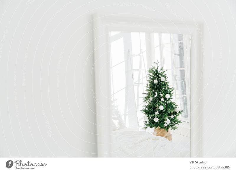 Decorated Christmas tree reflecting in mirror, white spacious room. Bedroom with New Year decoration. Modern classic style. Christmas eve at home christmas