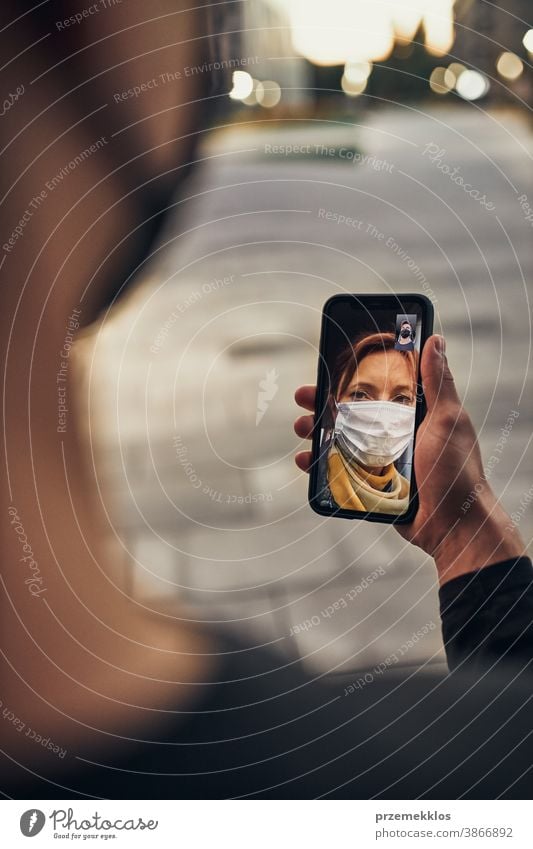 Young man having video call with her mother standing outdoors in the street in the evening wearing the face mask to avoid virus infection and to prevent the spread of disease in time of coronavirus