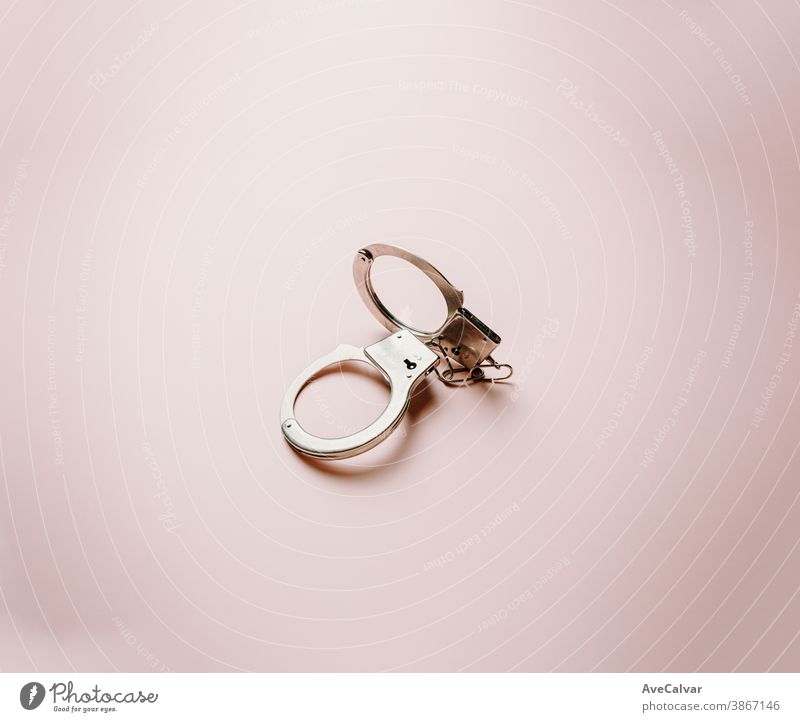 A pair of metallic handcuffs over a flat and bright pastel pink background administration applications authority being clipping path conceptual enforcement