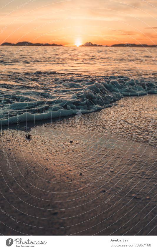 Vertical image of a tide on the beach over the sand during a colorful sunset with the islands as the background and copy space ocean wave sunrise gold surf