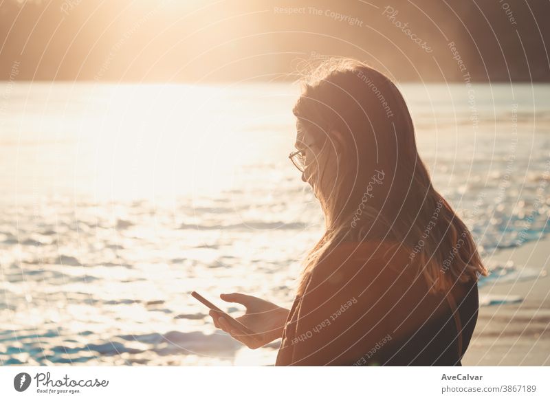 Young woman checking his cellphone in the beach during a sunset with copy space on colorful tones person smiling wireless holding technology internet laughing