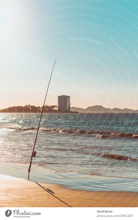 Fishing rod in a beach in front of a massive building during a sunset in spain ocean pole recreation sport horizontal reel surf angler men photograph game