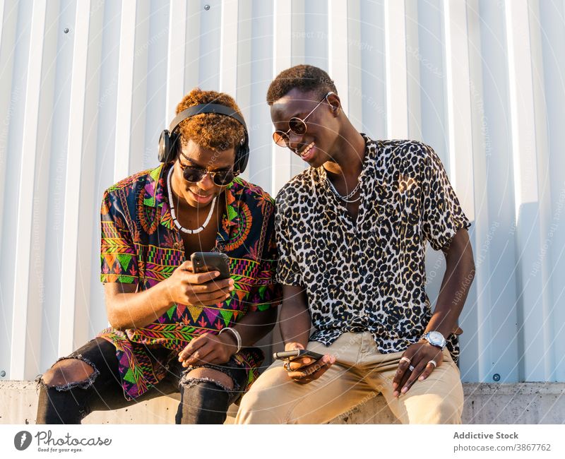 Positive young men looking at the mobile together in city friend style millennial smartphone trendy fashion ethnic black african american outfit fancy