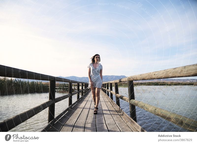 Woman in dress walking on wooden boardwalk woman footbridge lake summer confident path young female casual lifestyle vacation nature holiday lady freedom