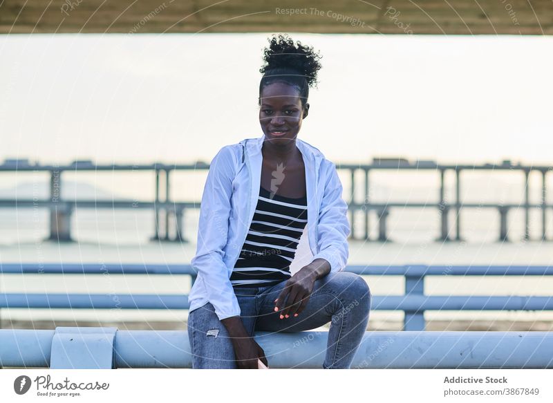 Happy ethnic woman resting on fence near sea embankment chill happy casual smile seafront railing young female african american black urban lifestyle cheerful