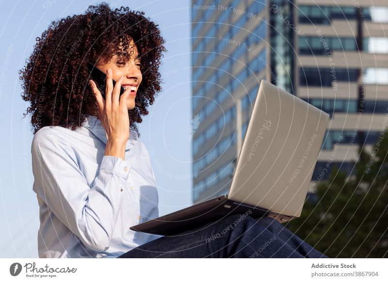 Charming ethnic freelancer working in urban park woman remote speak smartphone city multitask using female talk device gadget connection cheerful sit