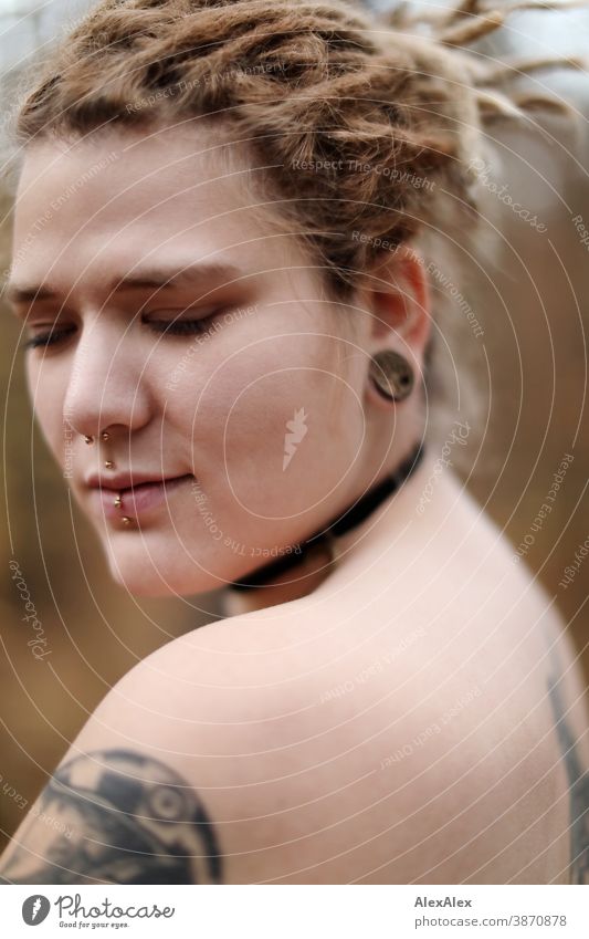 Lateral portrait of a young woman with dreadlocks and tattoos in the forest Woman Dirty Blonde tattooing Jewellery Piercing earring décolleté Upper body Naked