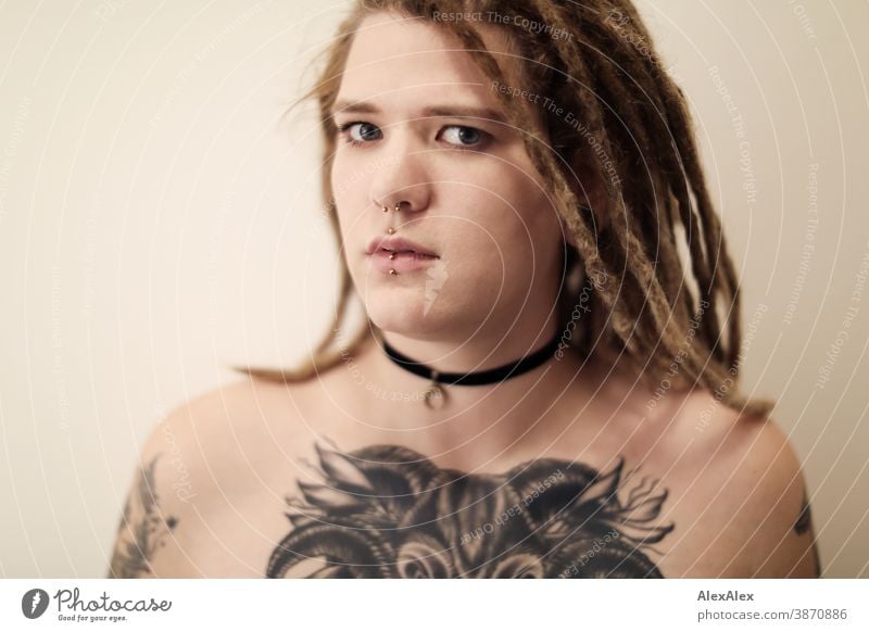 Portrait of a young woman with dreadlocks, who has a large tattoo of an ox head on her décolleté Woman Dirty Blonde tattooing Jewellery Piercing earring Chest