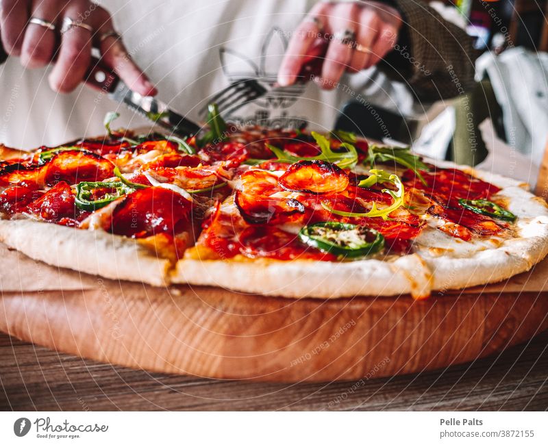 Tasty and delicious Italian salami pizza. Pizza fork knife tasty tasteful jalape cheese tomato tomato sauce wooden plate table eating dinner meal food